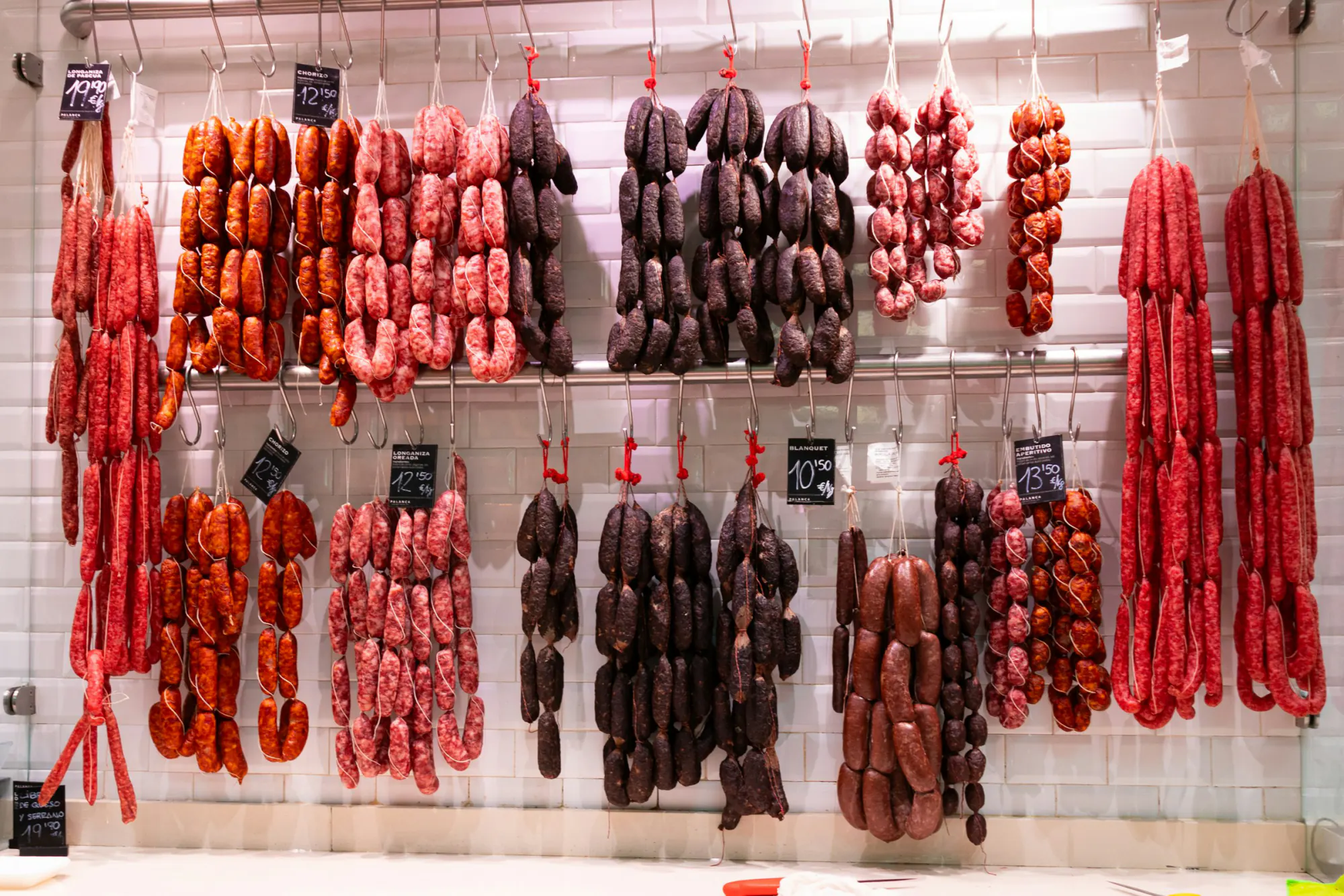 A deli wall of hanging sausages and chorizo with price cards