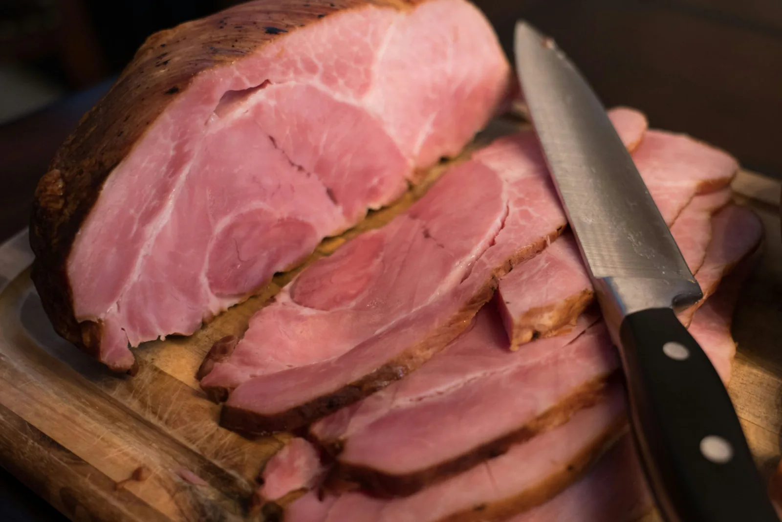A smoked ham on a wooden board, partly sliced